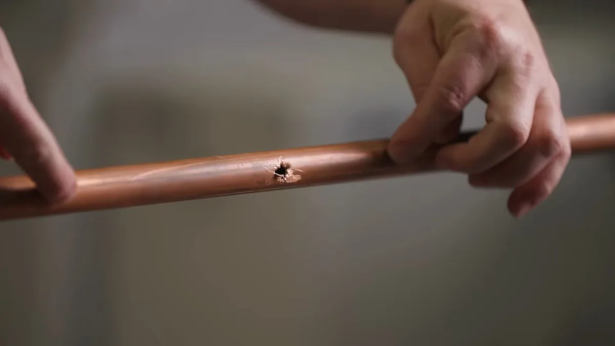 Hands holding a copper pipe with a small pinhole in its side.