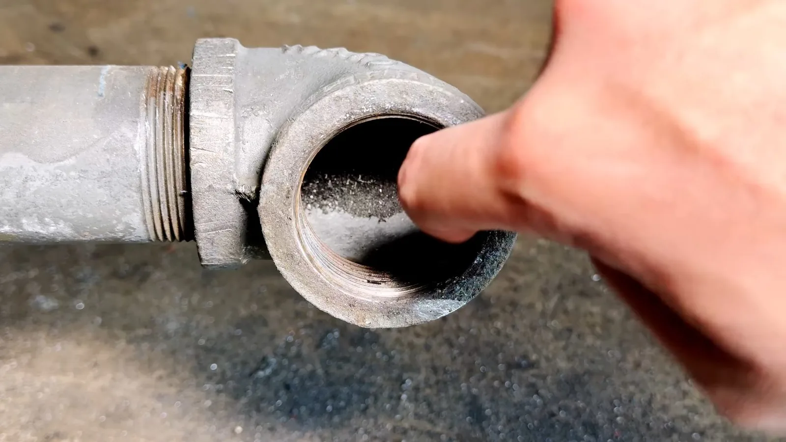 Finger resting at the open end of a galvanized cleanout fitting, with debris inside.
