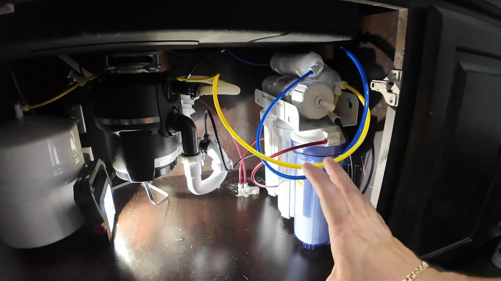 Under-sink cabinet showing a garbage disposal beside a reverse osmosis filter and tubing.