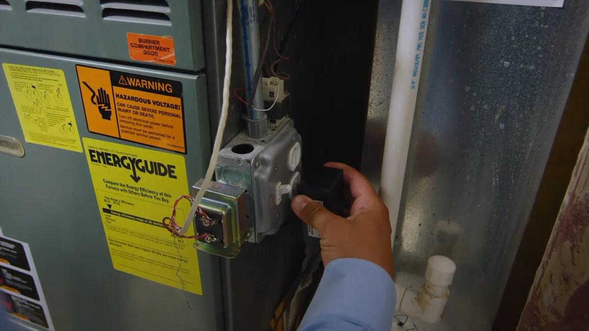 Hand reaching to a gas control and electrical box beside warning and EnergyGuide labels.