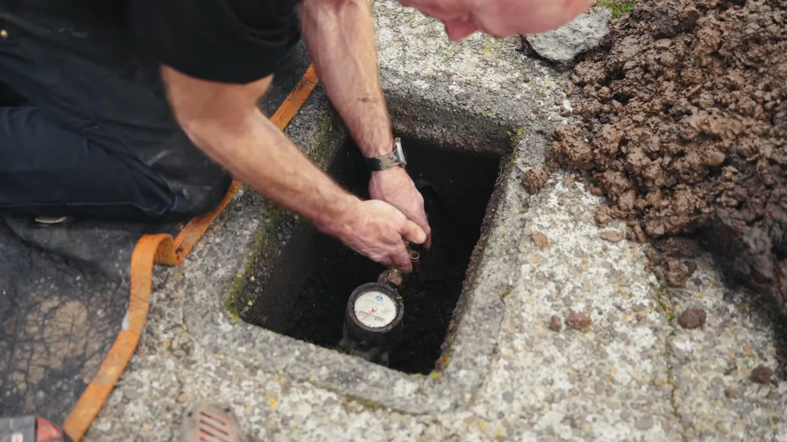 Man's hands reaching into a concrete box to read a water meter.