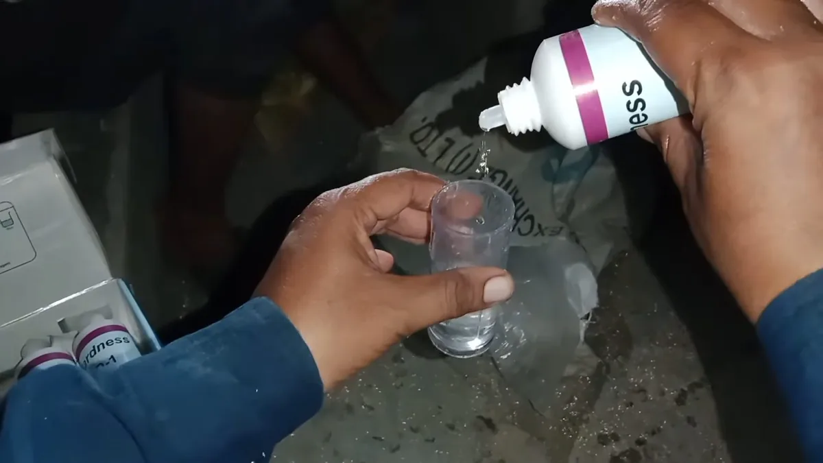 Hand adding drops from a test bottle into a small clear cup.
