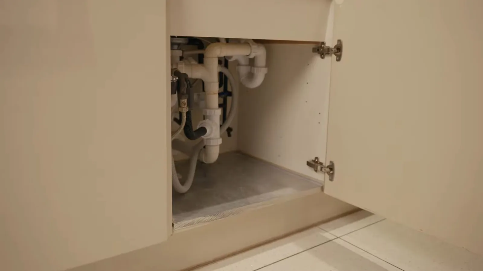 Open under-sink cabinet with a white drain trap and supply lines.