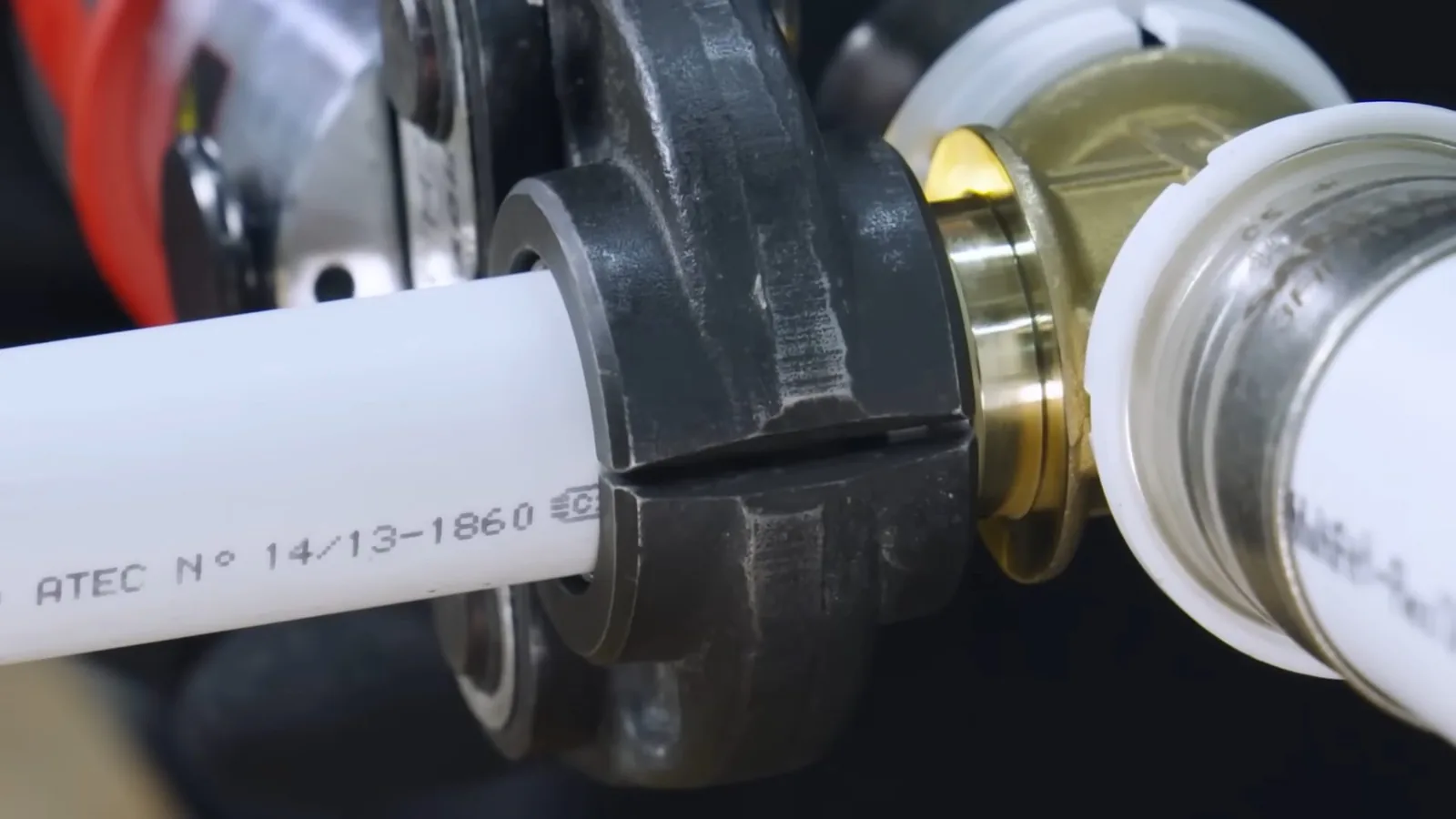 White PEX pipe held in a black press tool beside a brass fitting.