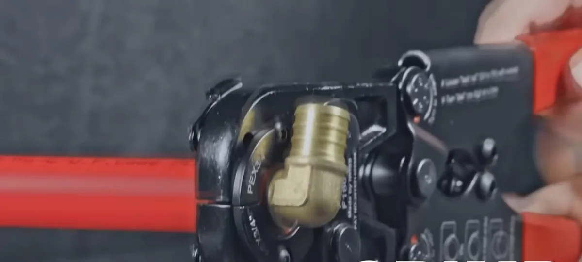 Press tool crimping a brass elbow onto red PEX pipe.