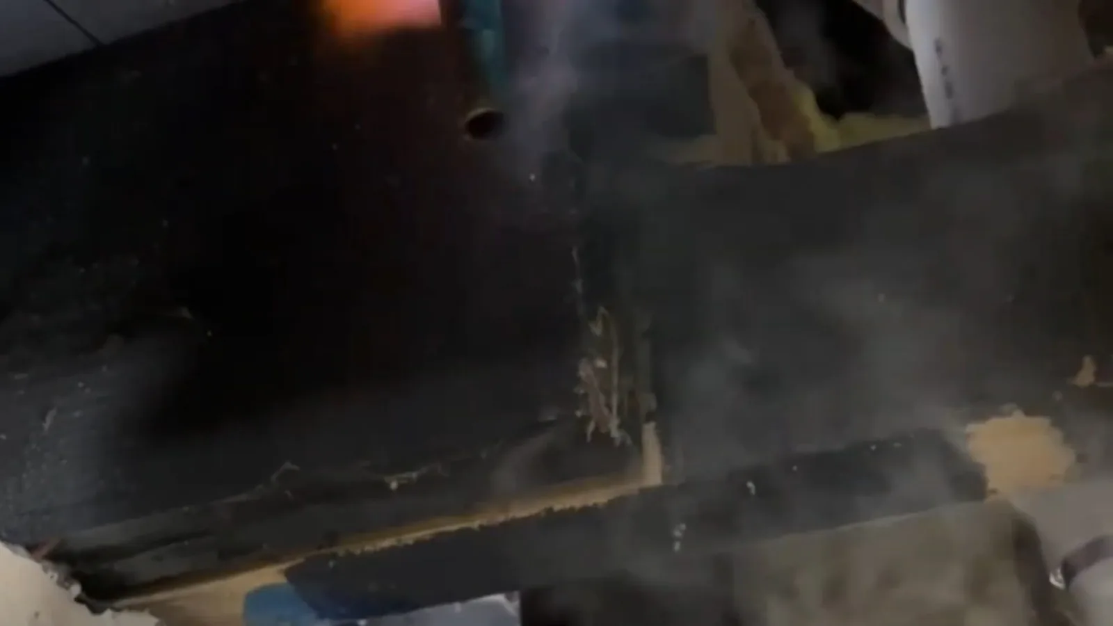 Steam rising around a dark wood beam beneath a floor.
