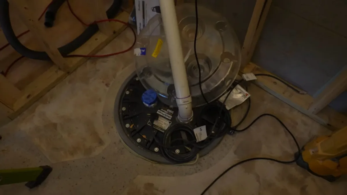 Round sump basin with a vertical white pipe set into a basement floor.