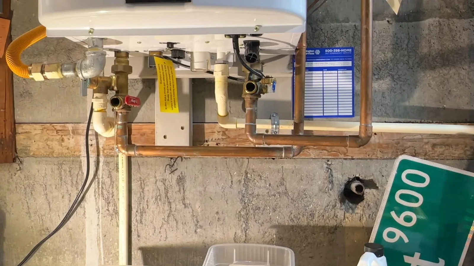 Wall-mounted tankless water heater with a yellow gas connector and copper lines with valves below it.