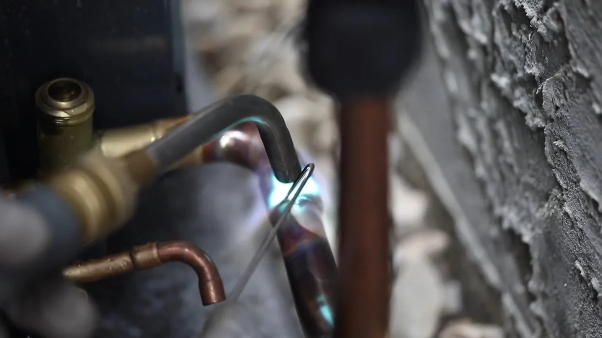 Torch flame heating a copper fitting at a water heater, with a brass valve beside it.