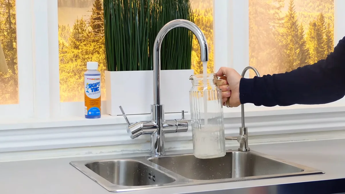 Water running from a chrome kitchen tap into a glass jar, with a small bottle on the counter.