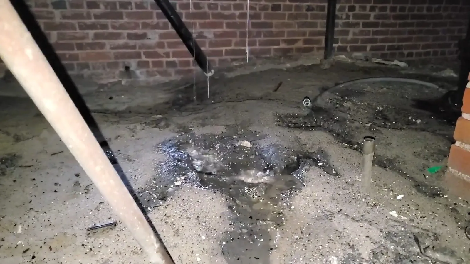 Dark, wet patch on a crawlspace floor beneath exposed pipes.